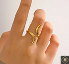 Gold crescent moon-shaped ring on a finger against a neutral background