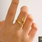 Gold crescent moon-shaped ring on a finger against a neutral background