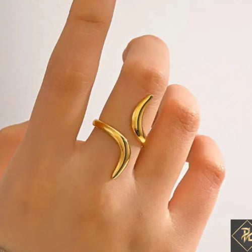 Gold crescent moon-shaped ring on a finger against a neutral background
