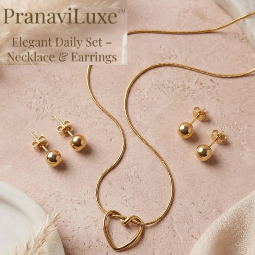 Gold necklace and earring set by PranaviLuxe, featuring a heart-shaped pendant on a snake chain and matching stud earrings, displayed on a textured pink surface.