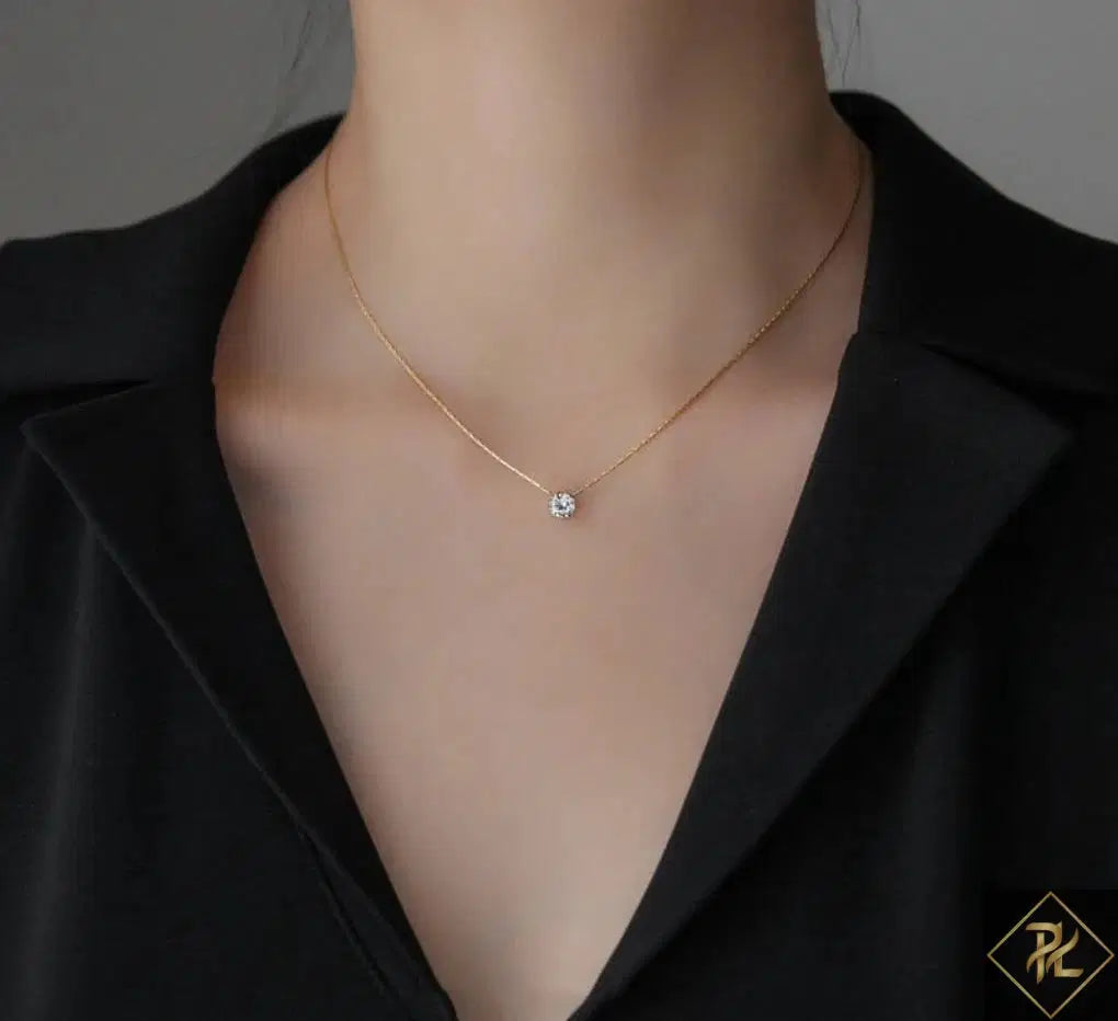 Gold necklace with a small pendant on a person wearing a black blazer.