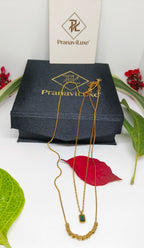 Green Stone Layered Necklace with delicate gold plated chains, featuring a small green stone pendant and a row of gold elements, displayed on a black PranaviLuxe box with natural leaves around.