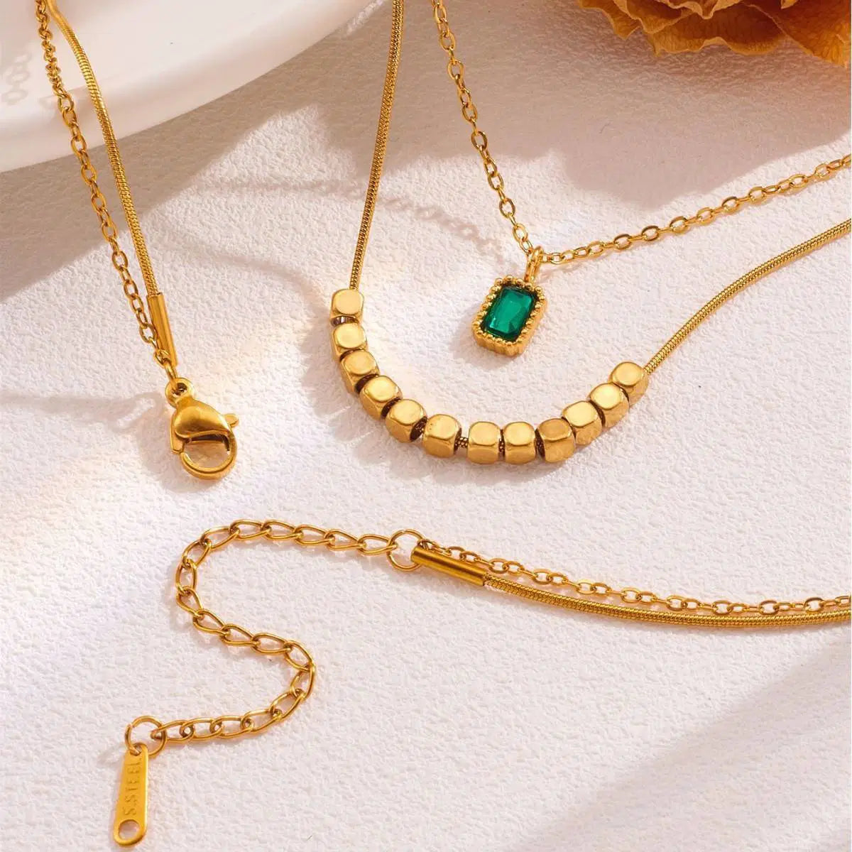 Green Stone Layered Necklace featuring delicate gold chains, a rectangular green stone pendant, and a row of small gold beads, styled as elegant modern fashion jewelry.
