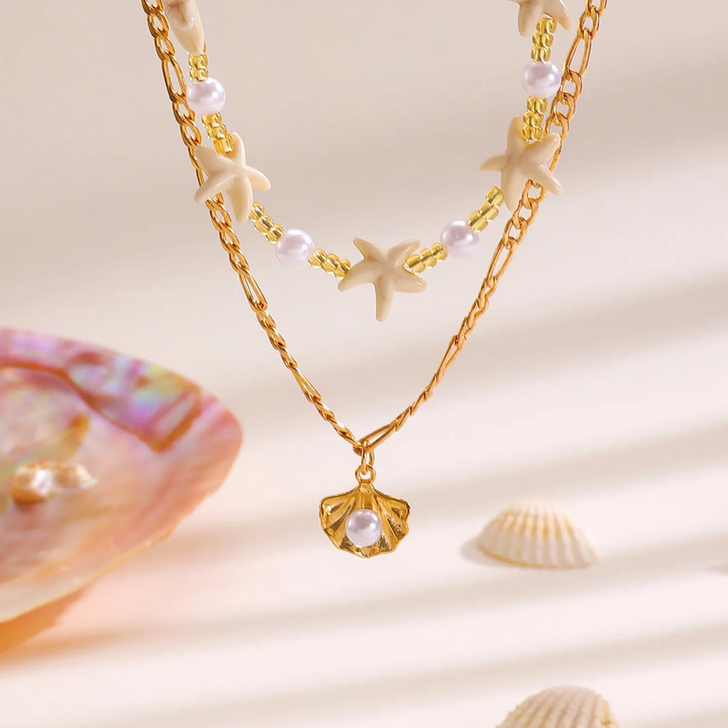 Gold chain necklace with shell pendant on a sandy background with seashells.
