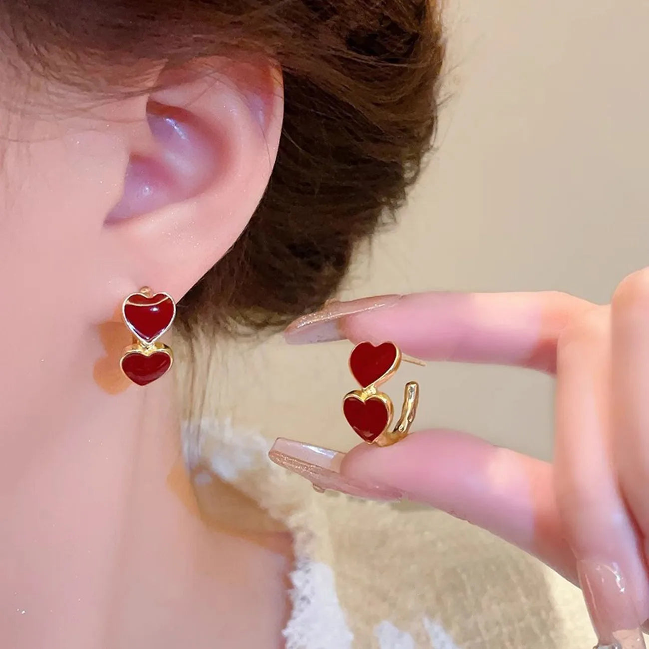 Red heart-shaped earrings being worn and held up to an ear.