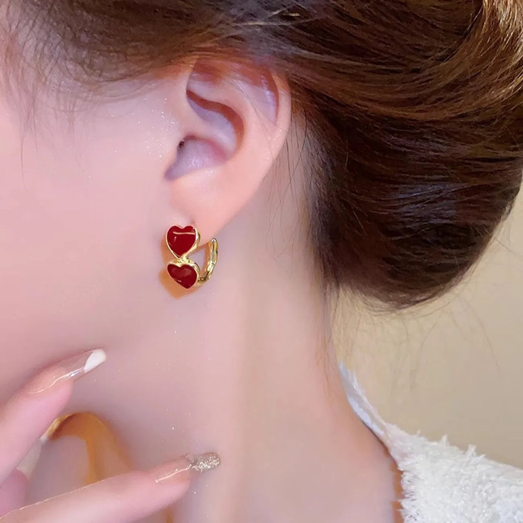 Close-up of a person wearing gold hoop earrings with red heart charms.