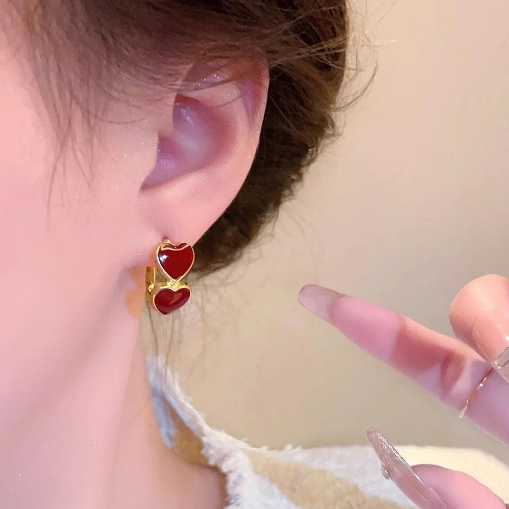 Red heart-shaped earrings worn by a person with a blurred background