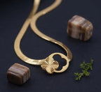 Gold necklace with a floral clasp on a dark surface with stones and moss.