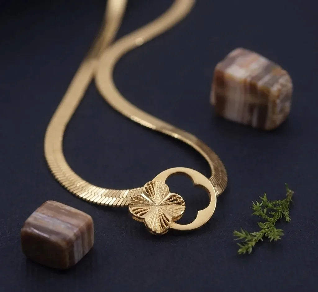 Gold necklace with a floral clasp on a dark surface with stones and moss.