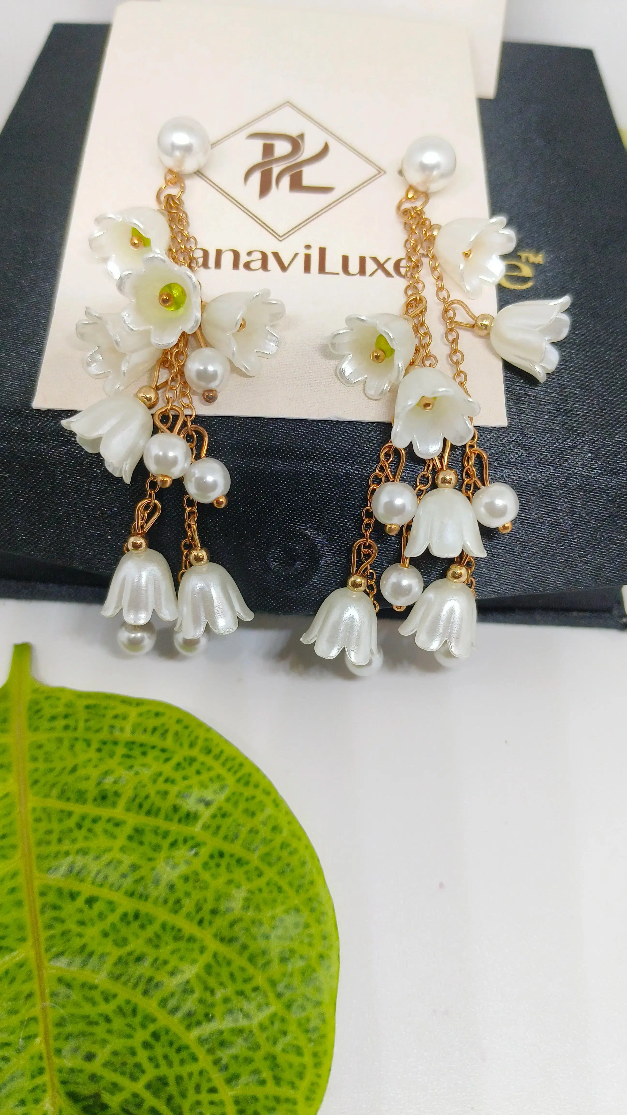 Floral earrings with pearl accents on a branded earring card, with a green leaf in the foreground.