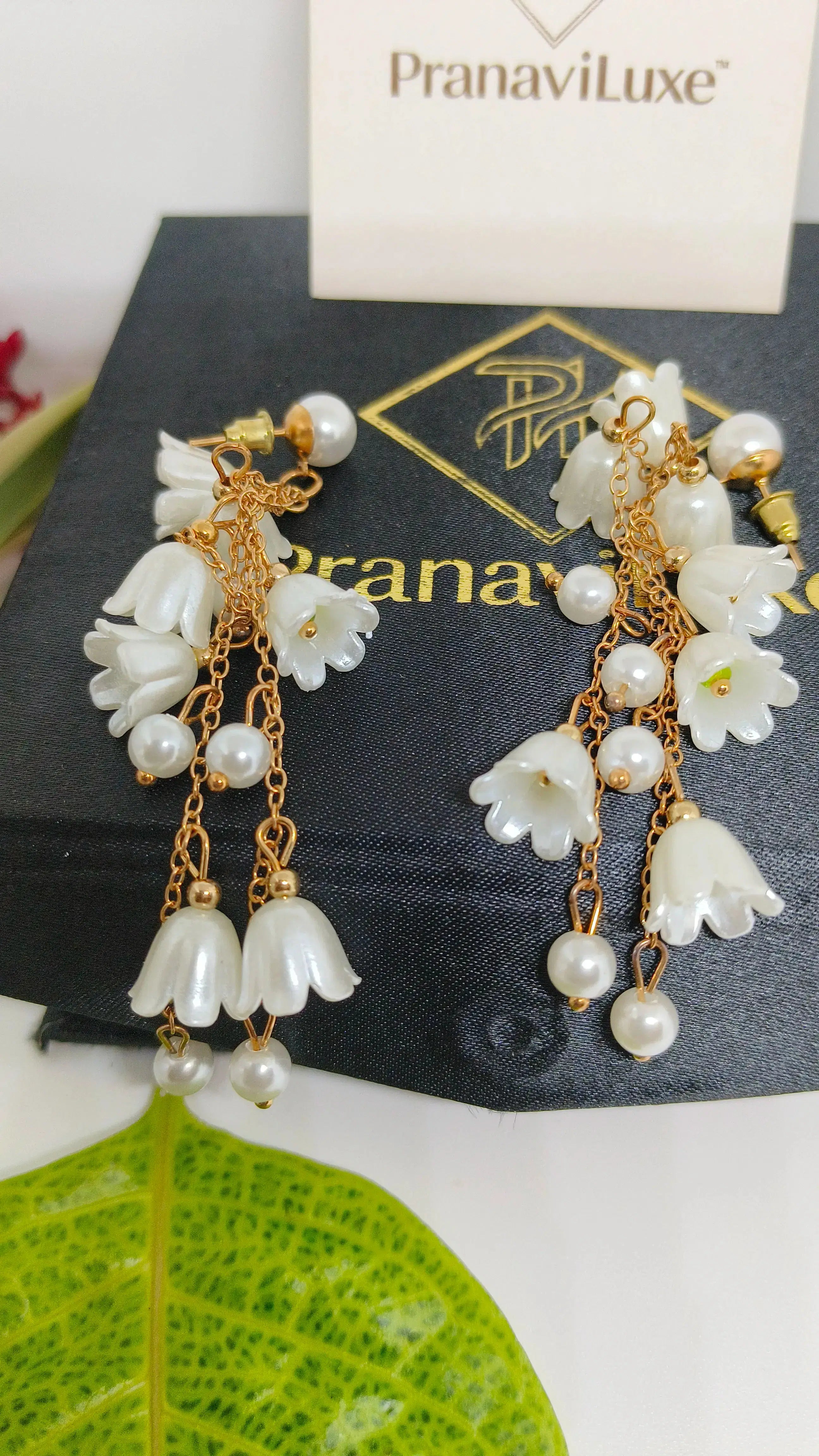 Pearl and gold earrings on a black card with 'PranaviLuxe' branding.