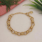 Gold bracelet on a light surface with greenery in the background