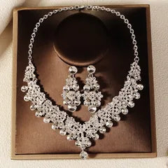 Silver necklace and earrings set in a brown box on a beige background