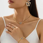 Woman wearing gold butterfly earrings, necklace, ring, and bracelet against a white background