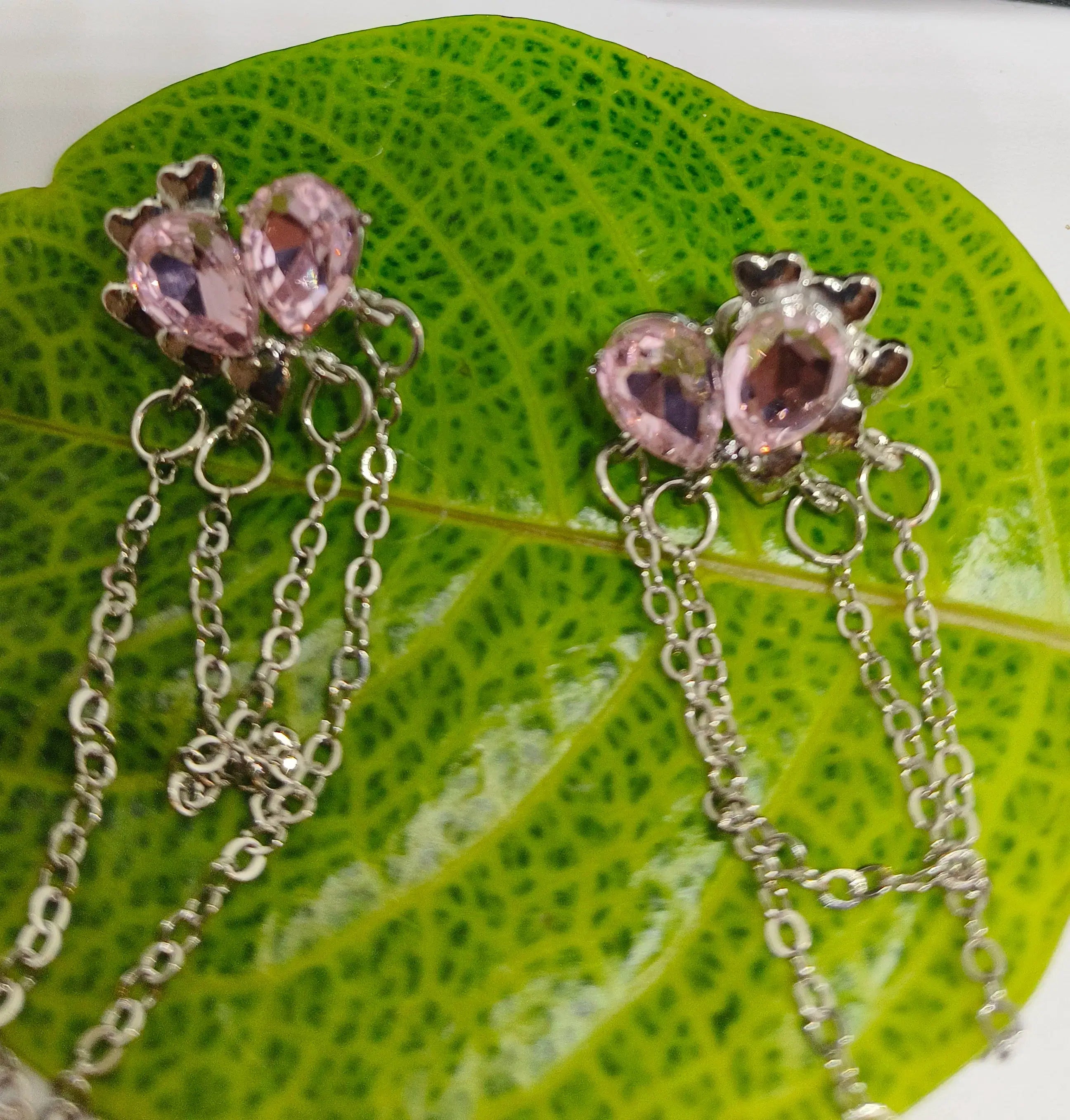 Pair of silver earrings with pink gemstones on a green leaf