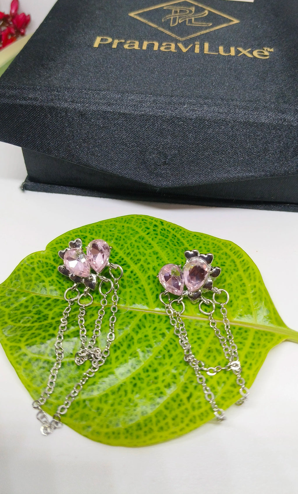 Silver earrings with pink gemstones on a green leaf, PranaviLuxe box in the background