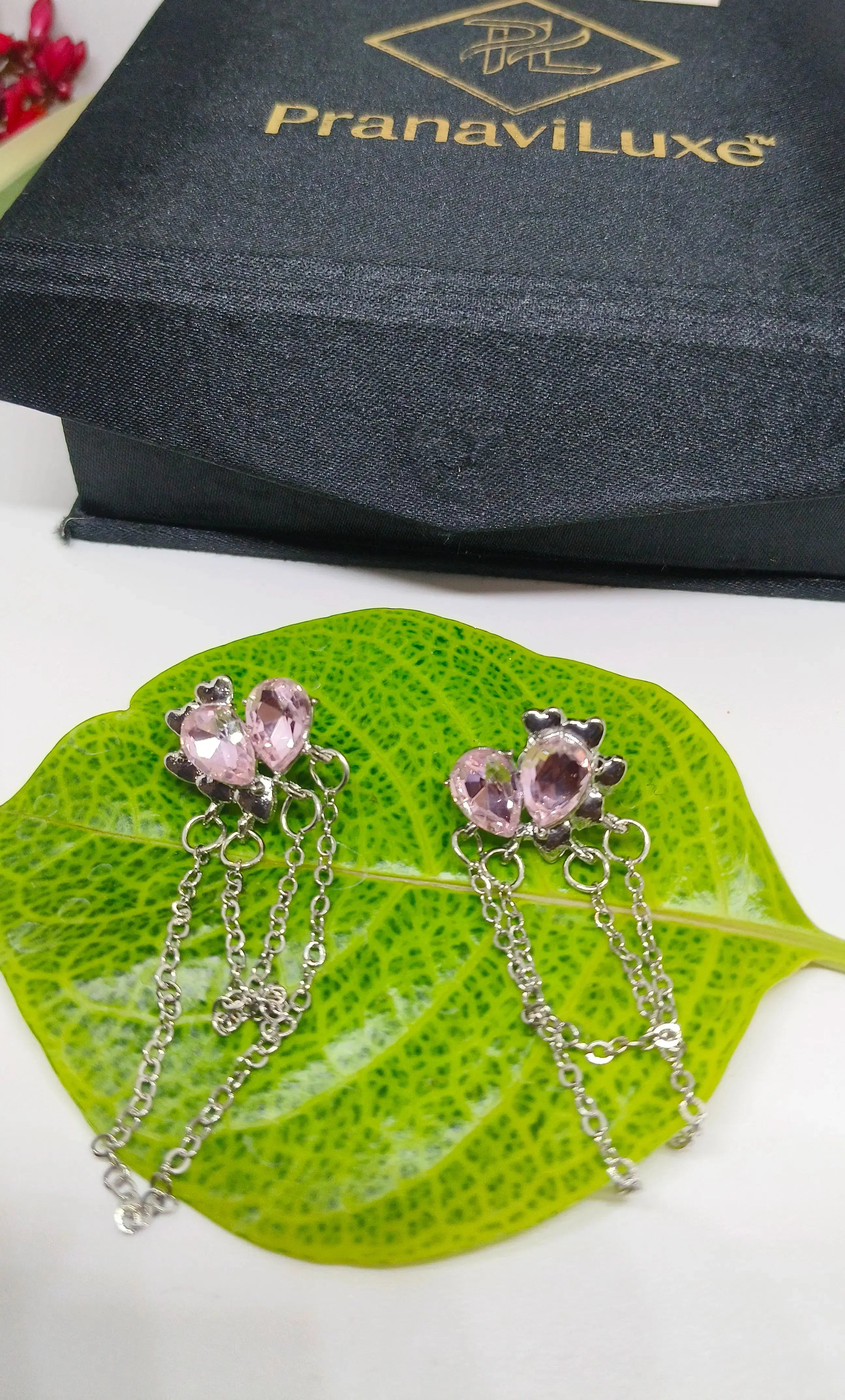 Silver earrings with pink gemstones on a green leaf, PranaviLuxe box in the background