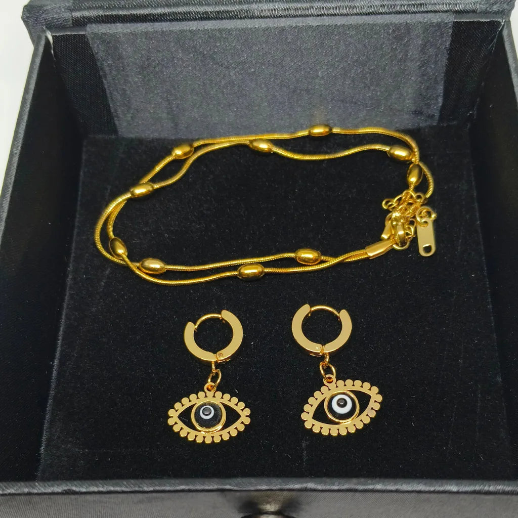 Gold-tone jewelry set including a beaded chain necklace and matching hoop earrings with evil eye charms, displayed in a black presentation box.