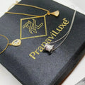 Gold and silver necklace jewelry displayed on a black branded box with the text 'Pranavi Luxe'. The jewelry includes a gold chain with a small gold heart-shaped pendant, a gold chain with a gold pendant, and a silver chain with a silver cylindrical pendant embellished with clear stones.