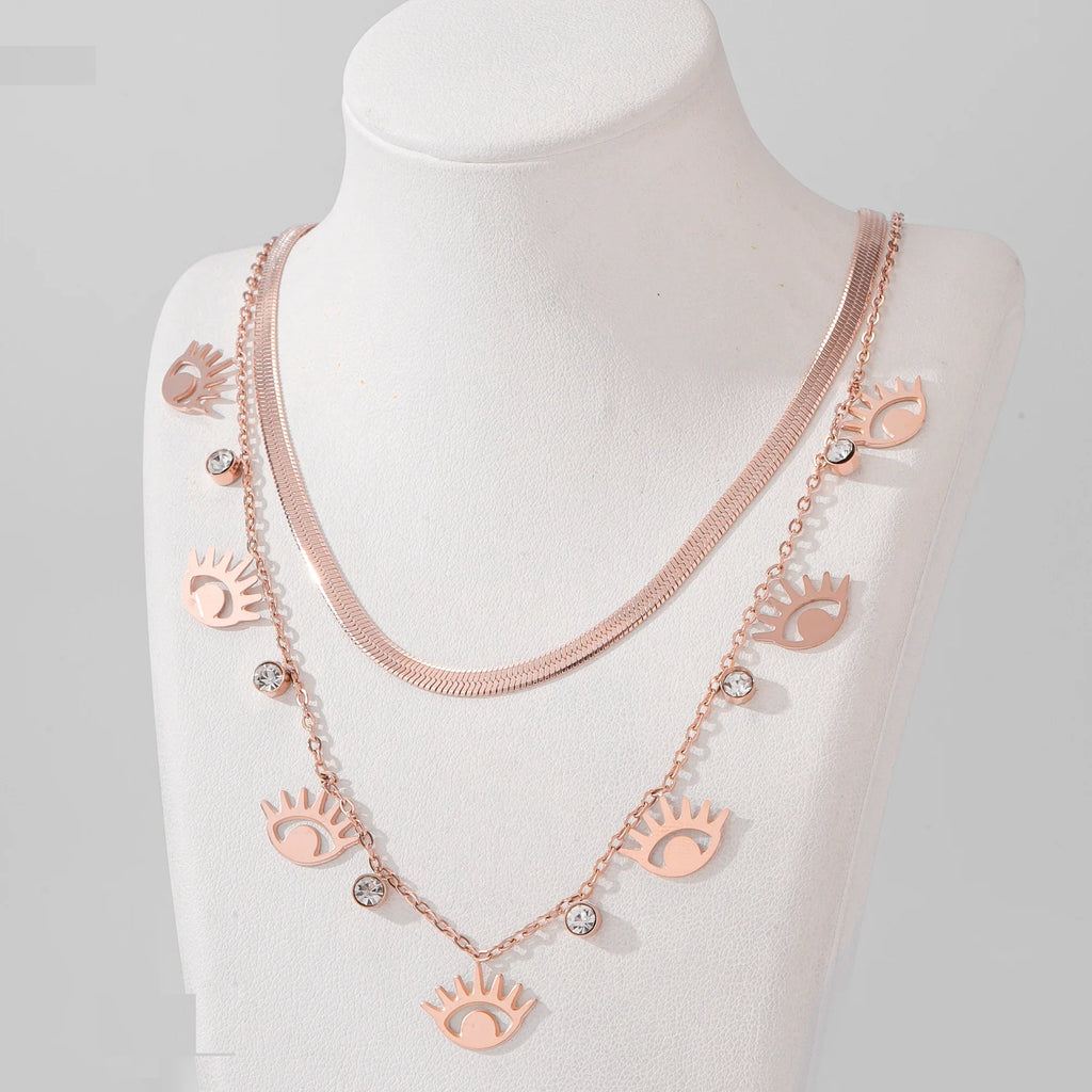 Rose gold necklace with eye-shaped charms on a mannequin against a gray background