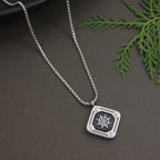 Silver necklace with a pendant featuring a ship's wheel design on a dark surface with green leaves.