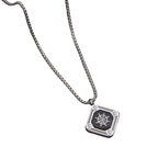 Silver necklace with a pendant featuring a ship's wheel design on a dark surface with green leaves.