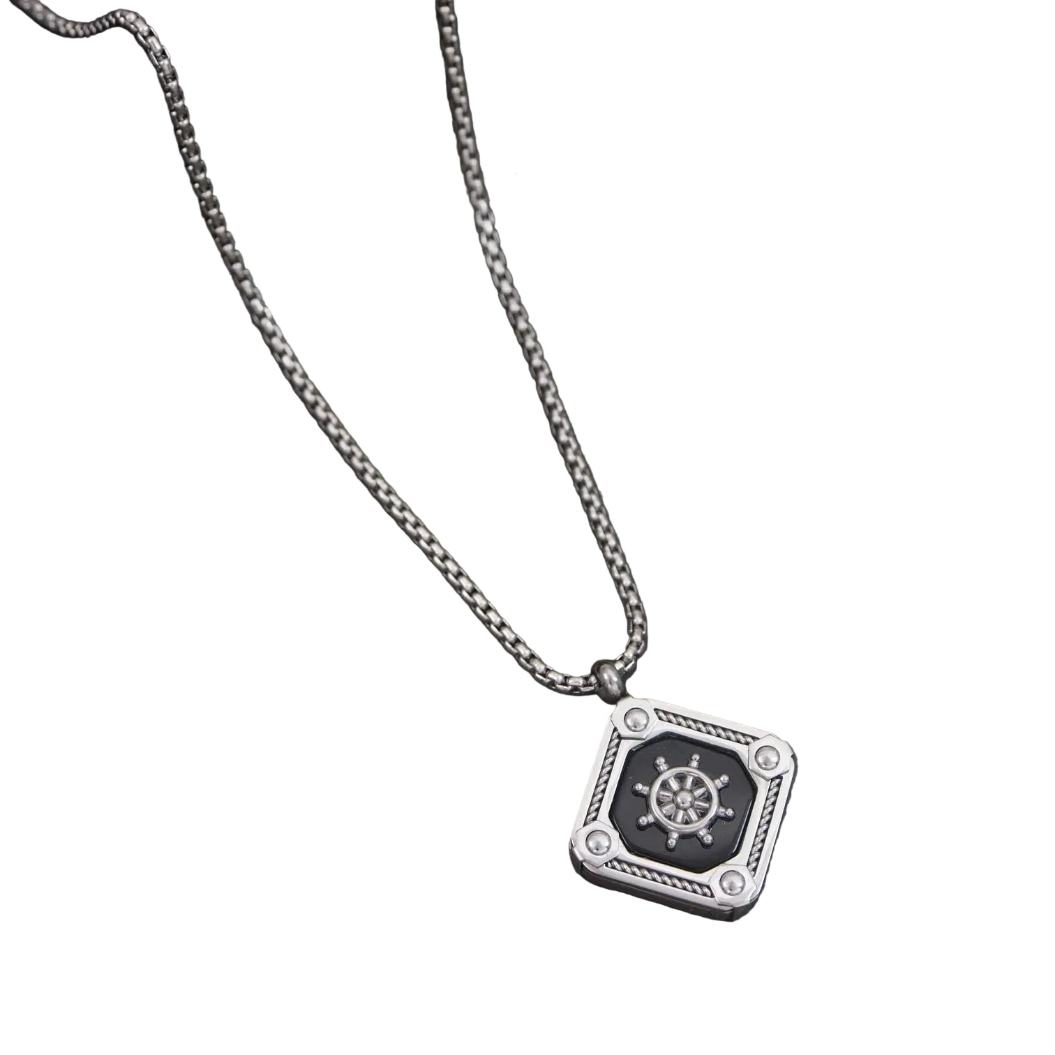Silver necklace with a pendant featuring a ship's wheel design on a dark surface with green leaves.