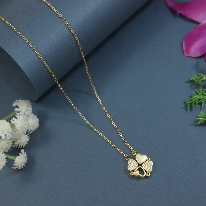 Gold necklace with a clover-shaped pendant on a blue background with flowers.