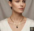 Woman wearing a gold necklace with a black pendant against a neutral background