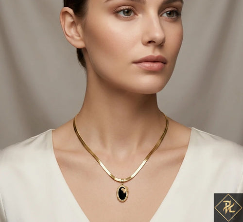 Woman wearing a gold necklace with a black pendant against a neutral background