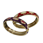 Two gold-plated bangle bracelets with colorful enamel patterns, one featuring red and cream motifs and the other purple and pink motifs, displayed on a white jewelry stand.