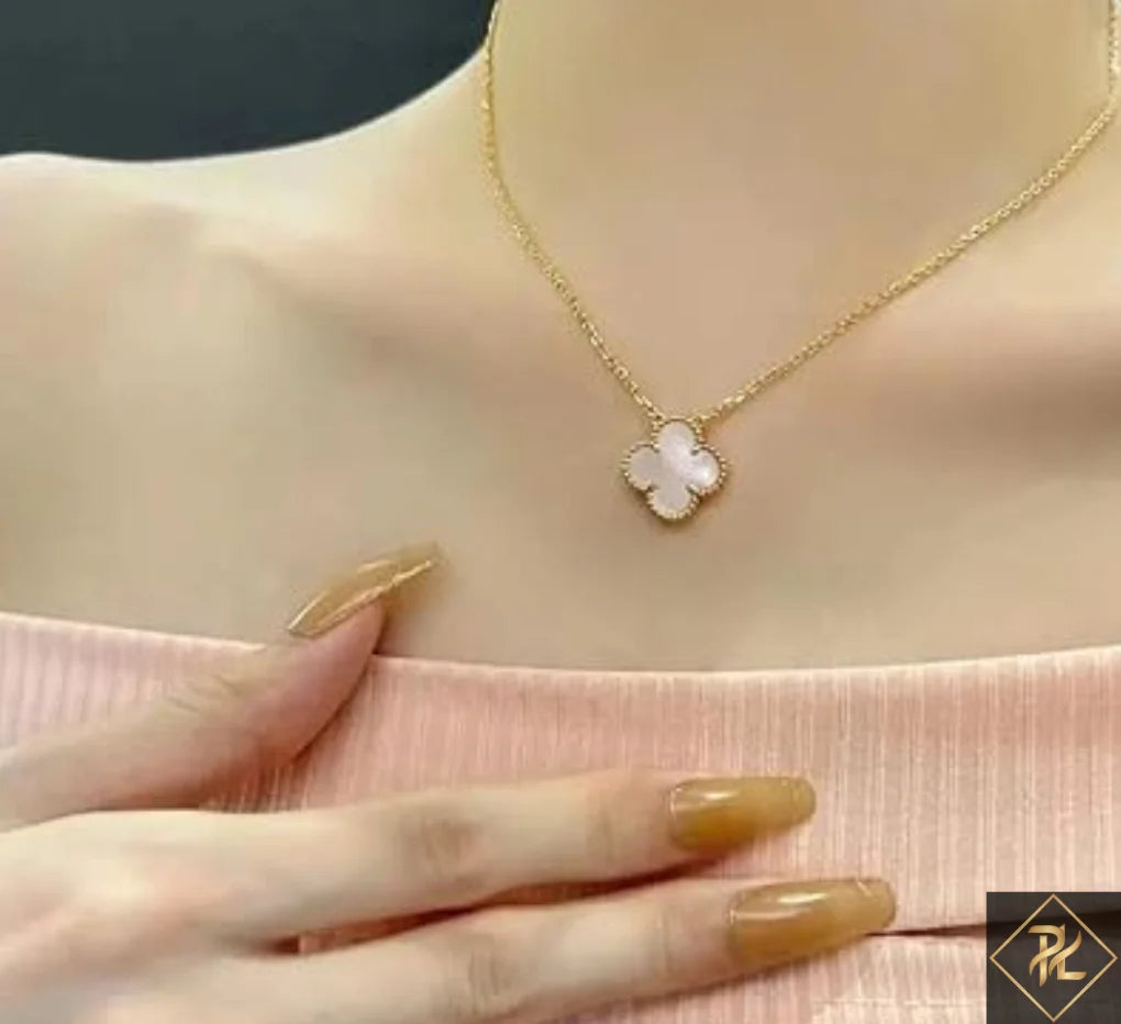 Gold necklace with a clover-shaped pendant on a person wearing a pink top.