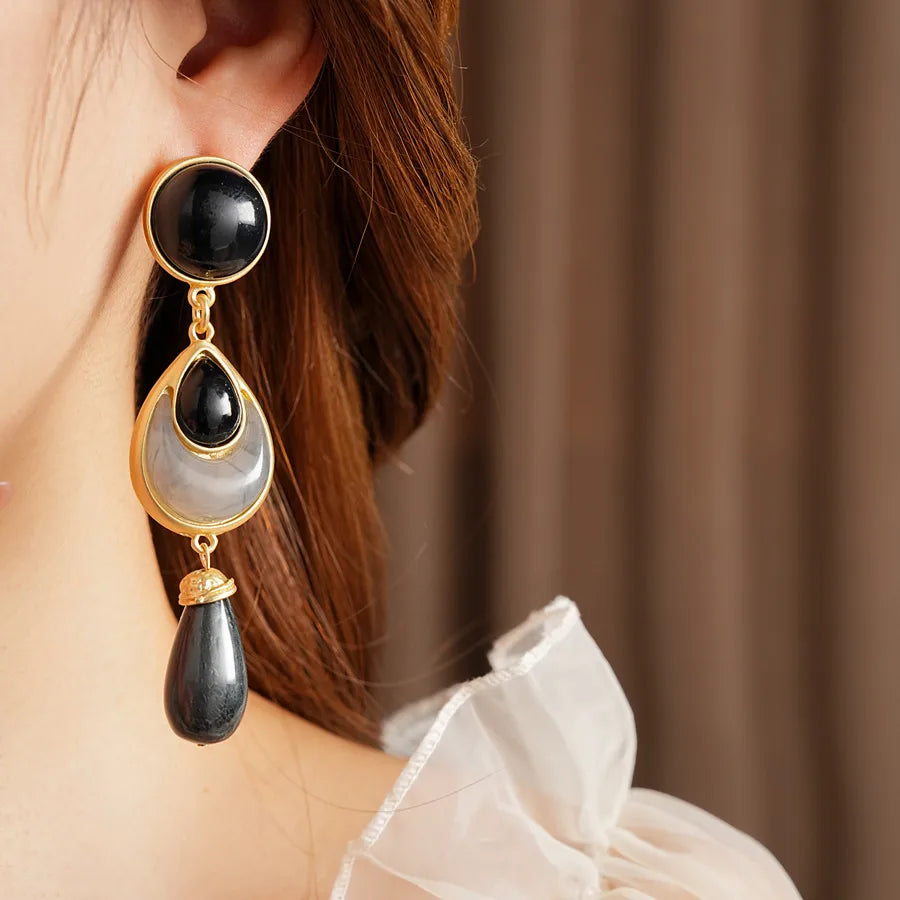 Close-up of a woman wearing elegant black and gold earrings with a neutral background.