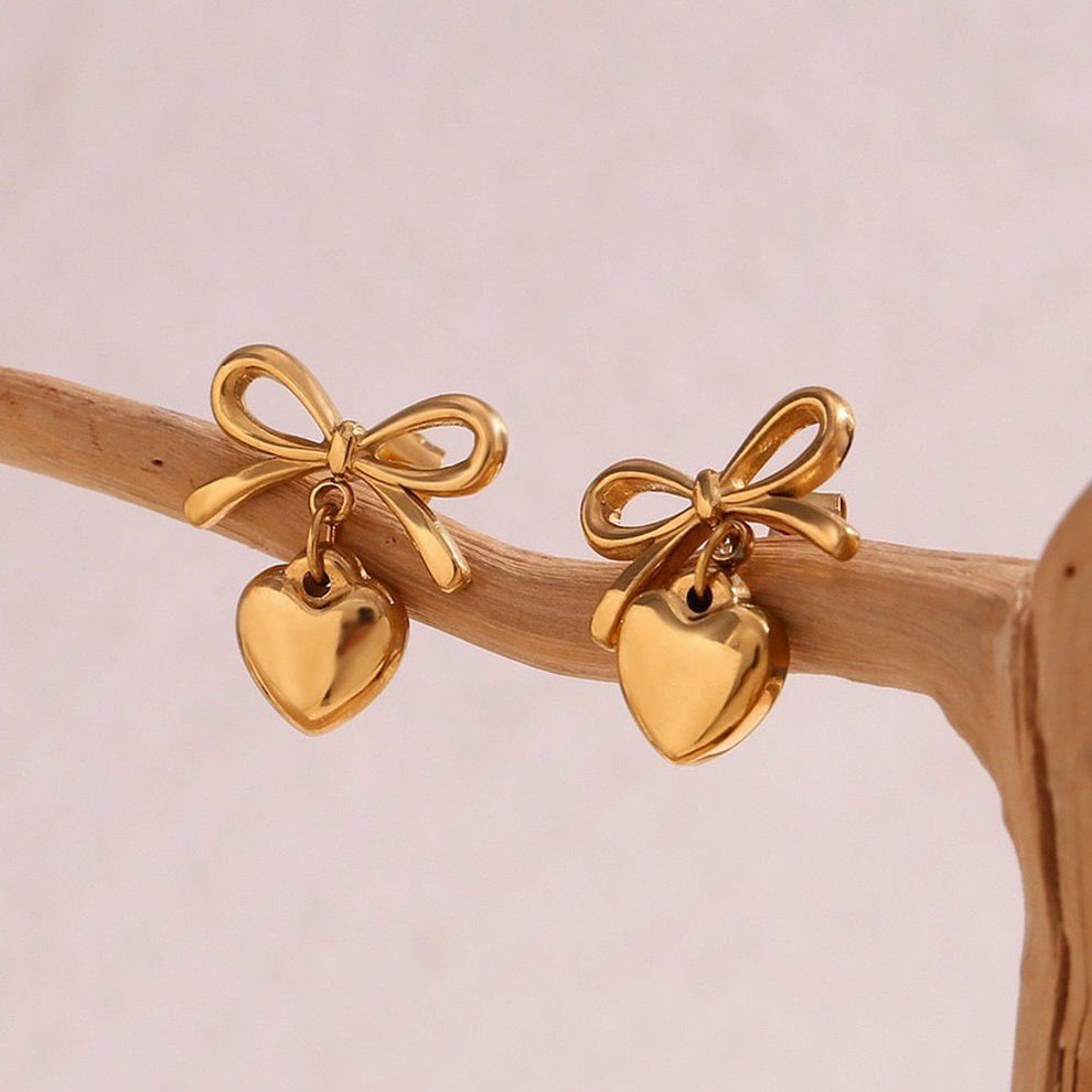 The Season of Bow Earrings stainless steel feature elegant gold-tone bows with dangling heart charms, perfect for stylish earrings lovers seeking modern fashion jewelry.