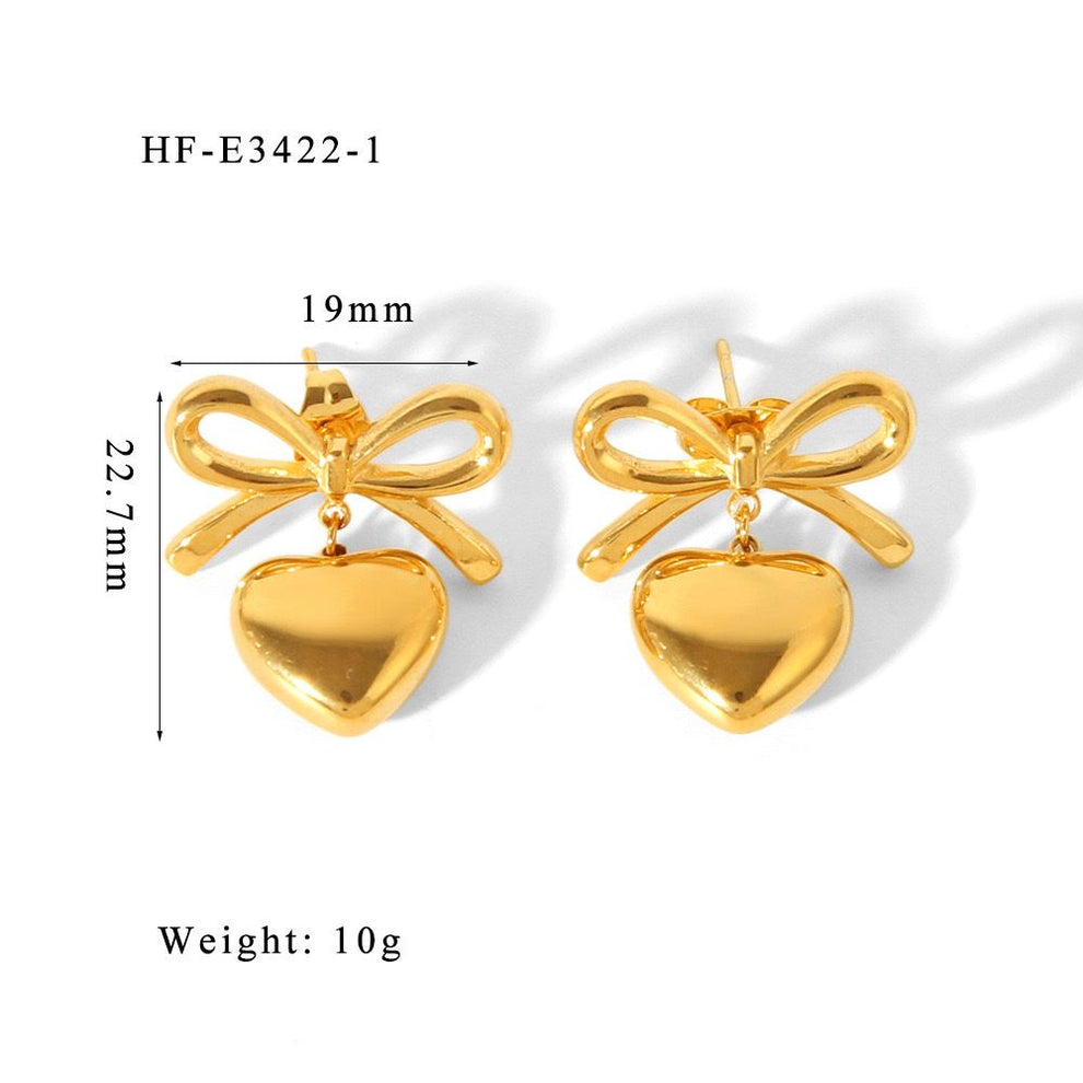 The Season of Bow Earrings stainless steel in polished gold tone featuring bow-shaped studs with dangling heart charms, lightweight and elegant fashion jewelry.