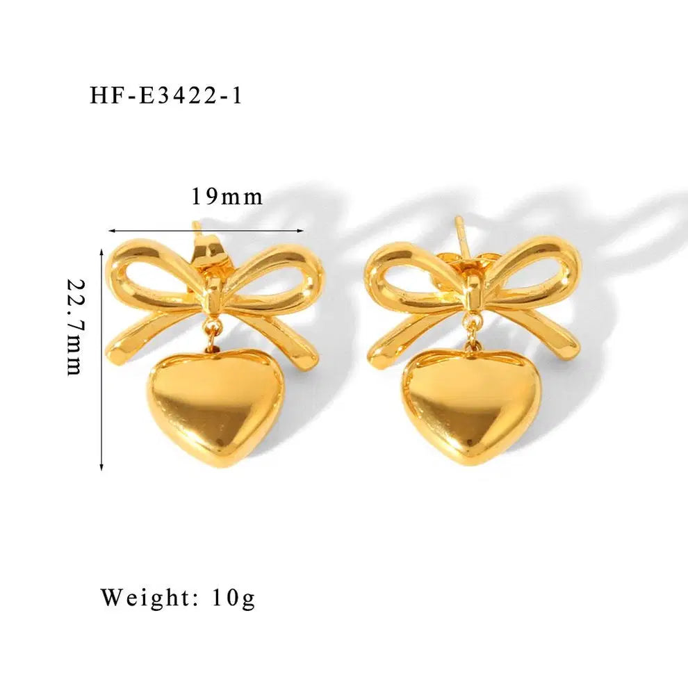 The Season of Bow Earrings stainless steel in polished gold tone featuring bow-shaped studs with dangling heart charms, lightweight and elegant fashion jewelry.
