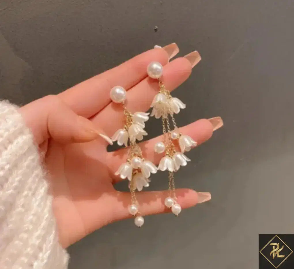 Hand holding a pair of floral earrings with pearl accents against a neutral background