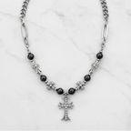 A silver-toned chain necklace with black beads, silver cross charms, and a central cross pendant, displayed on a white marble background.