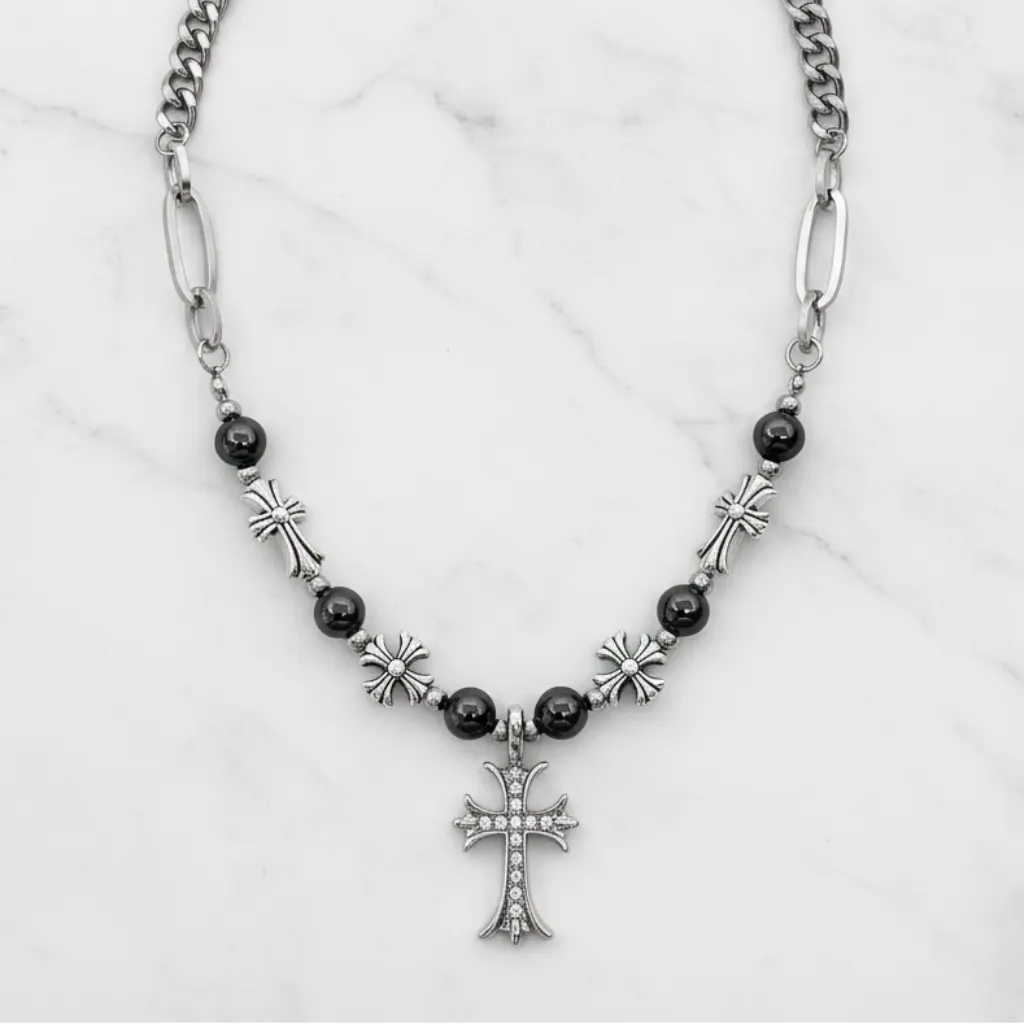 A silver-toned chain necklace with black beads, silver cross charms, and a central cross pendant, displayed on a white marble background.