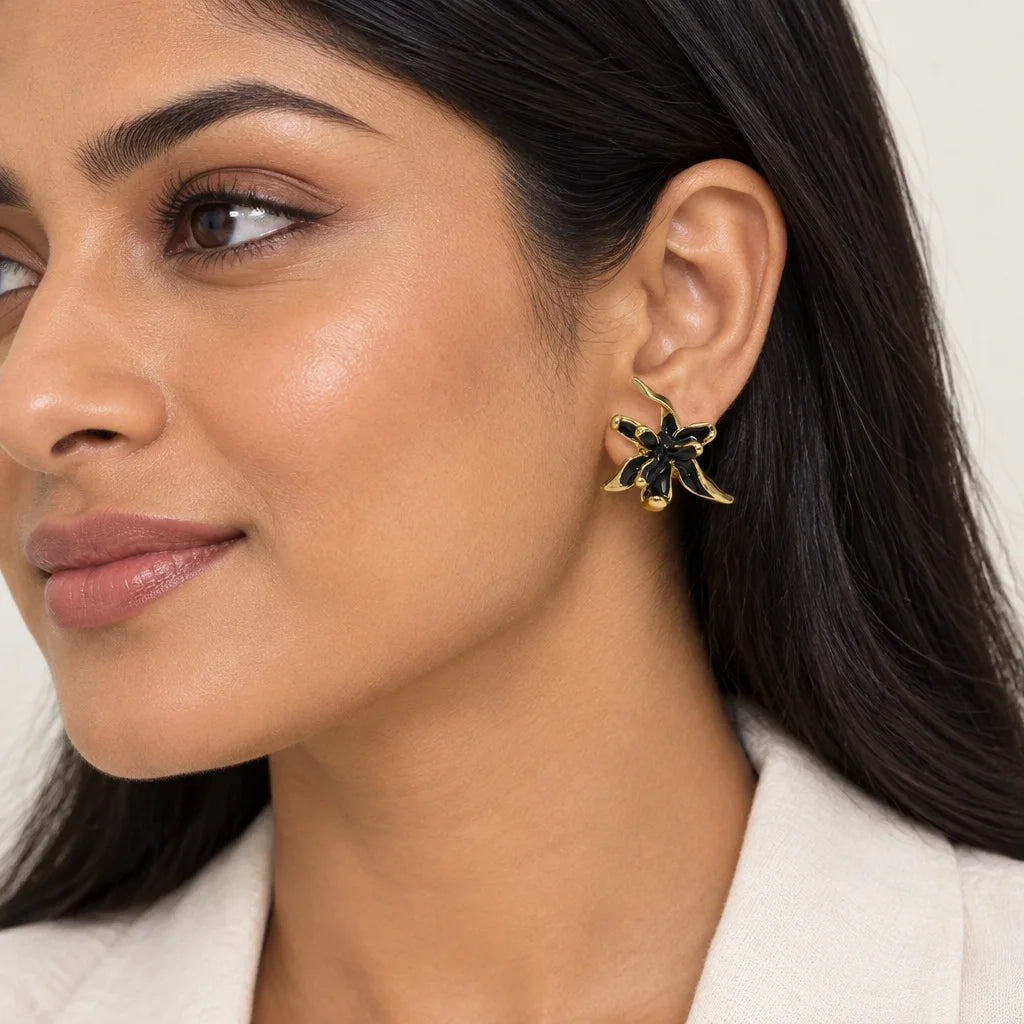 A close-up of a woman wearing a gold and black flower-shaped stud earring, showing the earring on her ear against a clean light background.