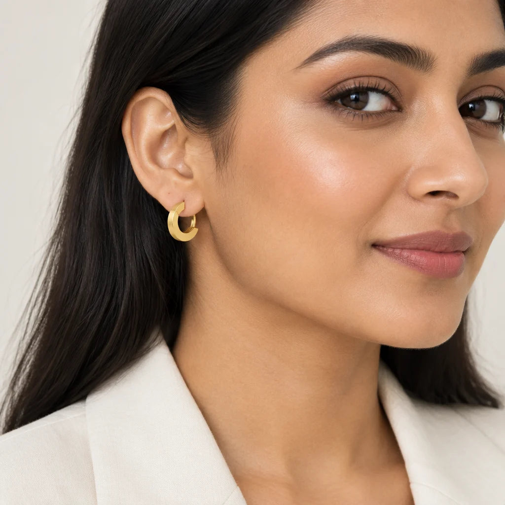 A close-up of a woman wearing a small gold crescent-shaped hoop earring, shown from the chest up against a soft light gray background.
