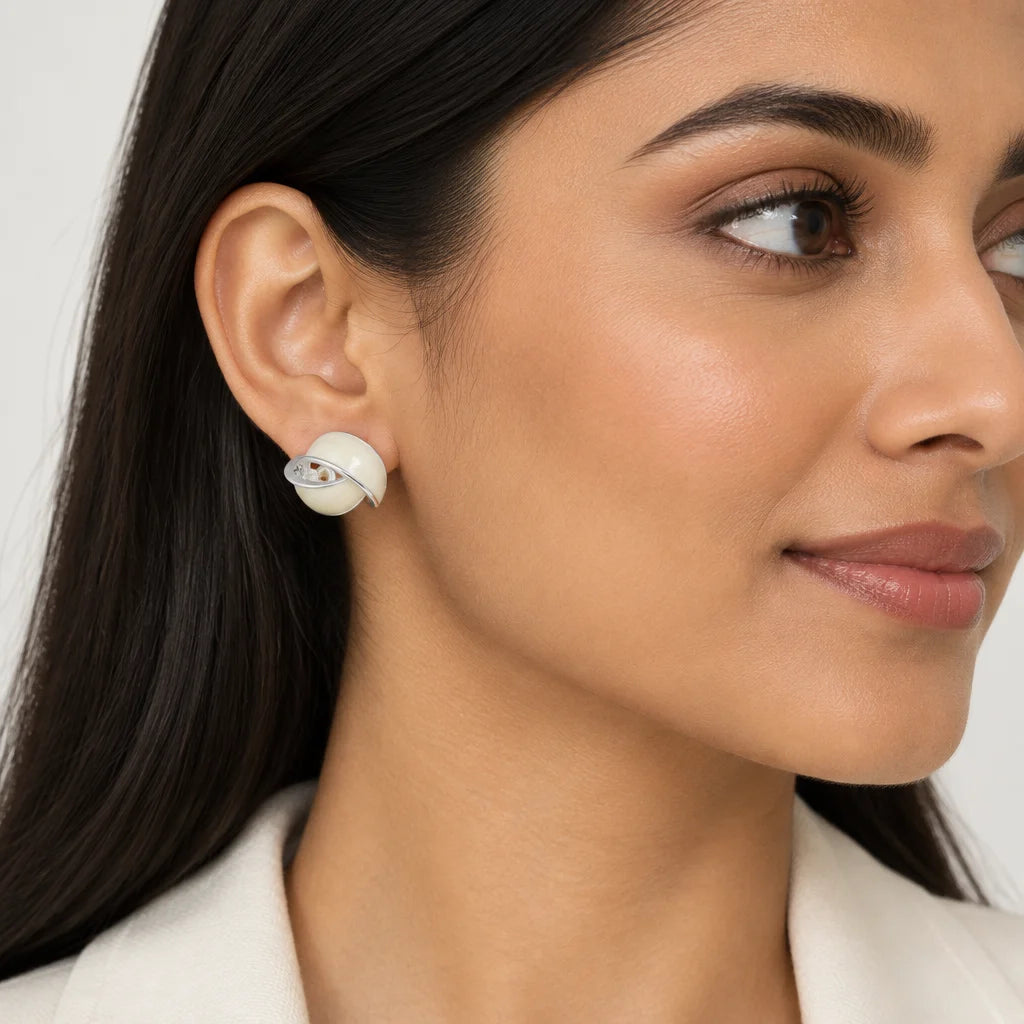 A close-up of a woman's ear wearing a small white spiral stud earring with a tiny silver gemstone accent, set against a clean light gray background.