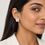 A close-up of a woman wearing a small square stud earring with a white and gray marbled pattern on a silver-toned base, set against a clean light background.