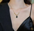Gold necklace with a black pendant worn by a person in a black outfit.