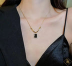 Gold necklace with a black pendant worn by a person in a black outfit.