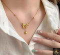 Gold necklace with heart and bow design worn by a person in a white shirt.
