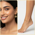 A split image showing a woman wearing a gold eye-shaped drop earring on her ear and a model's foot wearing a matching gold anklet on her ankle, set against a clean white background with a beige border.