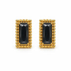 A pair of gold rectangular stud earrings featuring a faceted dark black gemstone in the center, surrounded by a border of small gold beads, set against a plain white background.