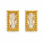 A pair of gold rectangular stud earrings featuring a faceted clear crystal center, surrounded by a raised beaded gold border, set against a plain white background.