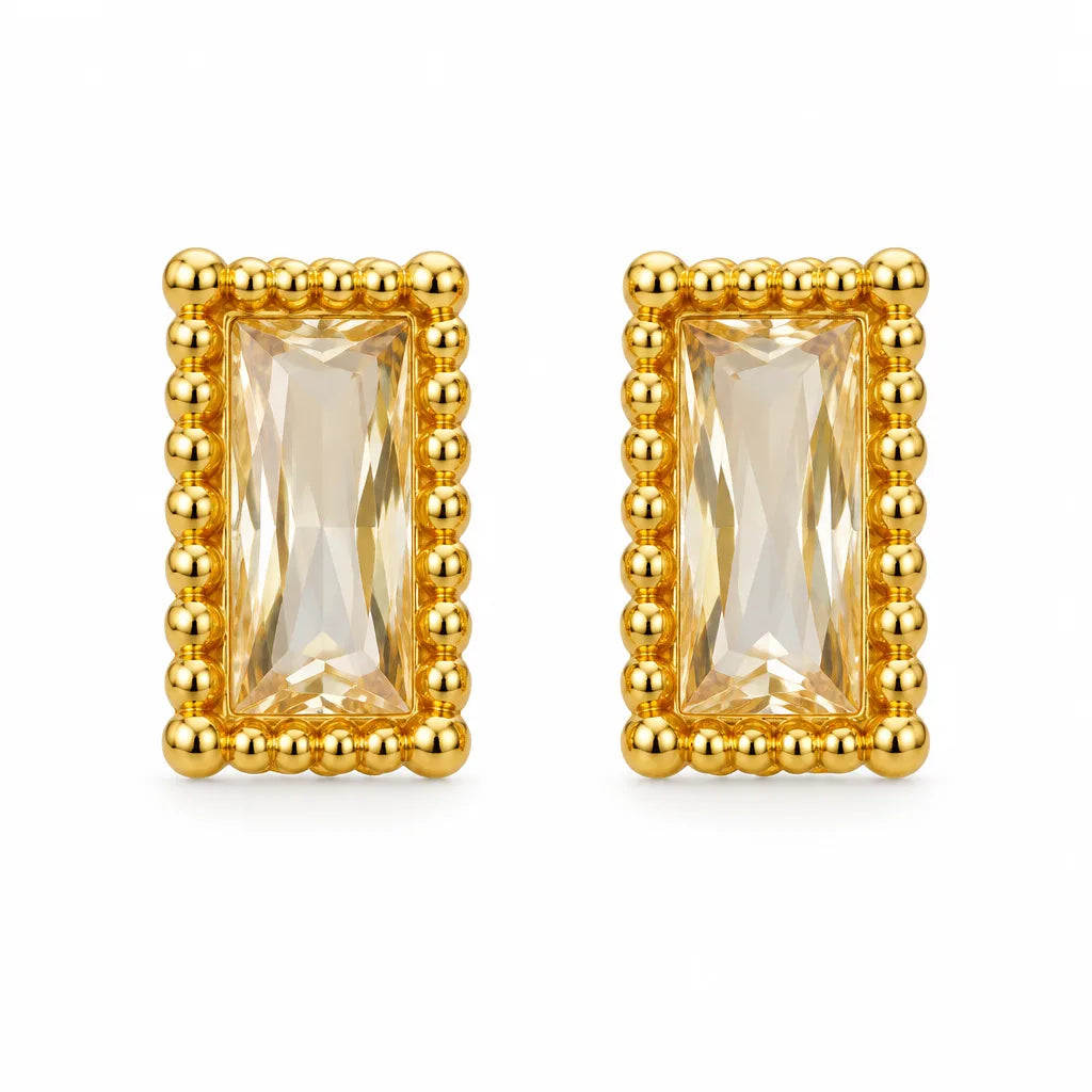 A pair of gold rectangular stud earrings featuring a faceted clear crystal center, surrounded by a raised beaded gold border, set against a plain white background.